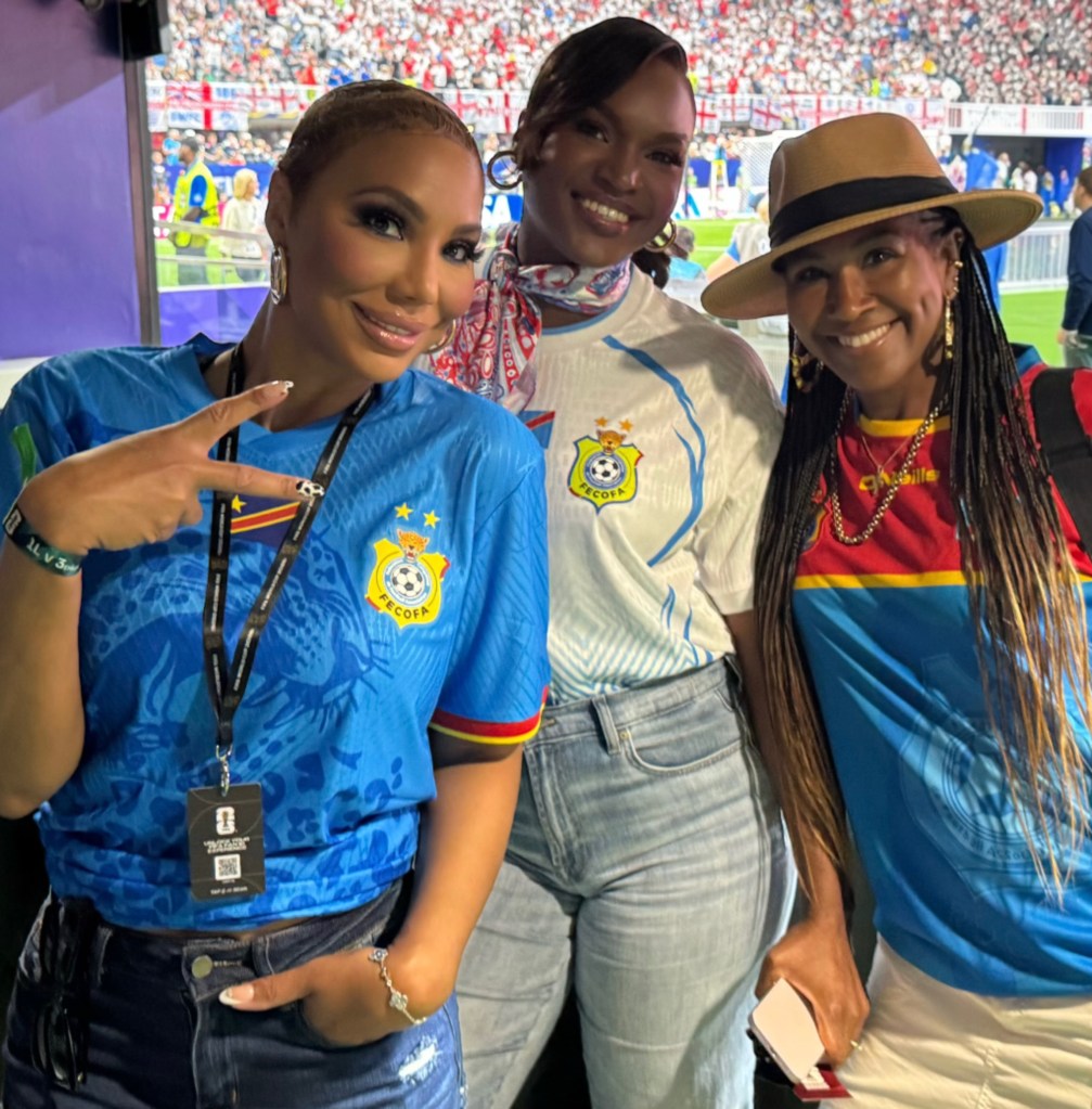 Three women in soccer jerseys and hats at a crowded stadium during the 2026 World Cup