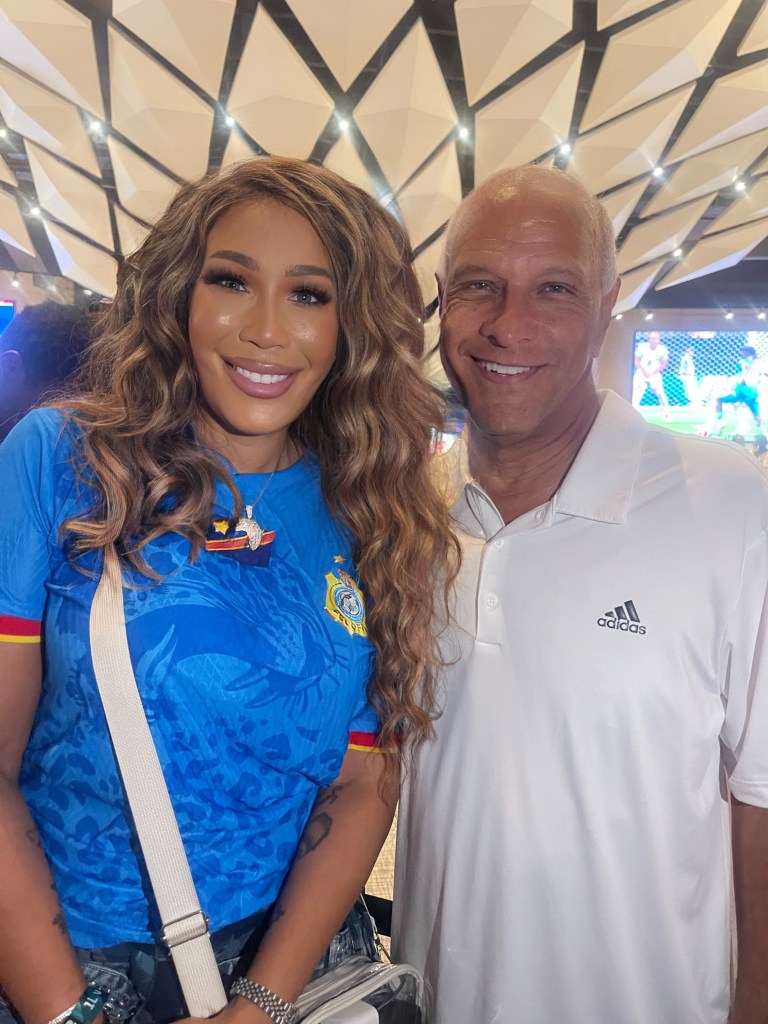 Two people posing in front of a patterned backdrop at a World Cup 2026 event in Atlanta